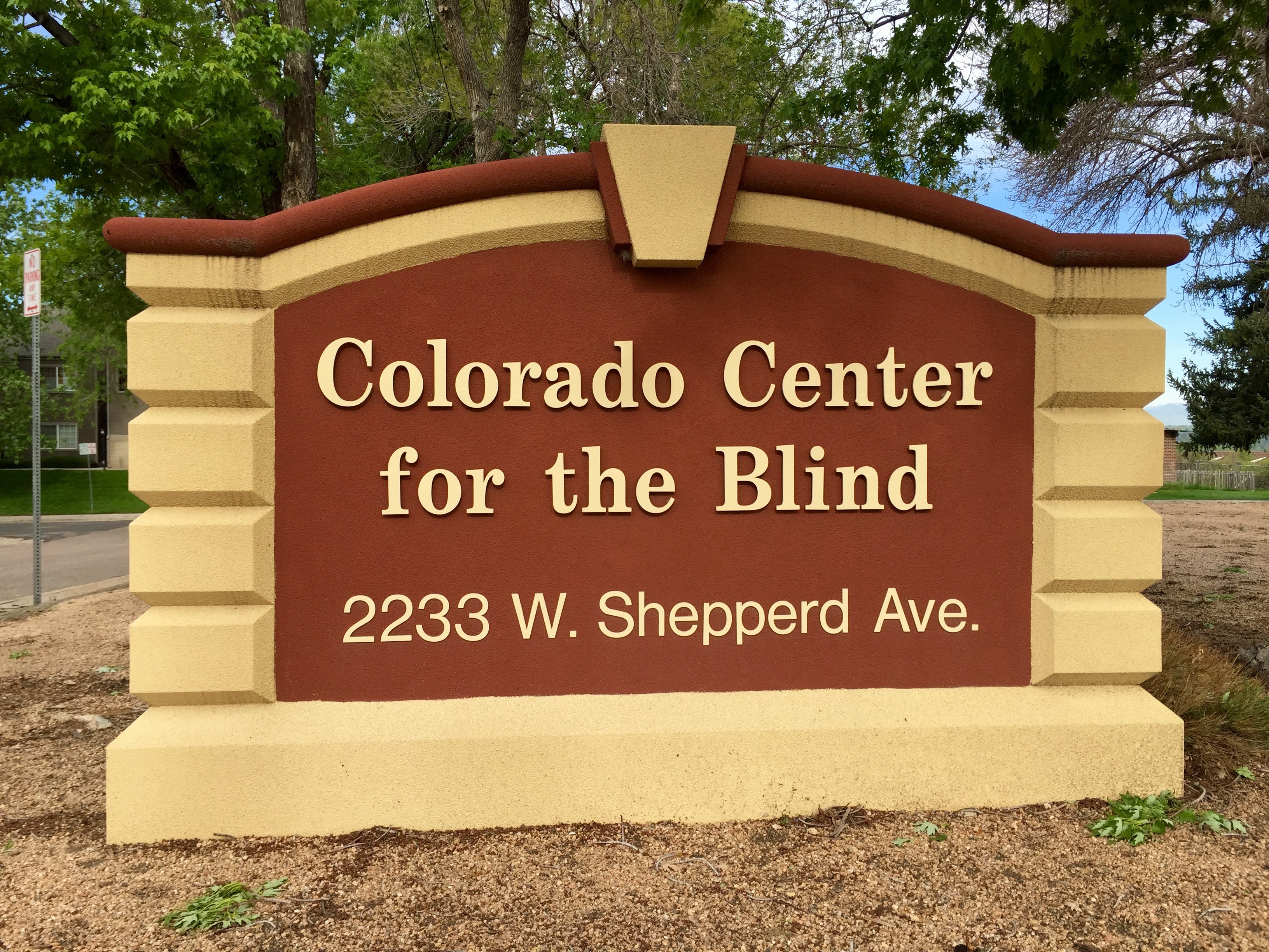 A large sign made of composite material that looks like stone, featuring beige and terracotta red coloring, reads “Colorado Center for the Blind” and “2233 W. Shepperd Ave.”