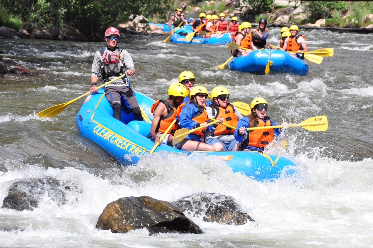 Four rafts navigate down Clear Creek toward some white water near some large rocks